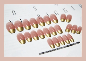 Détail de faux ongles amande rose nude avec pointes French dorées élégantes