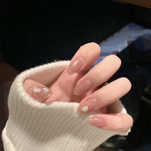 Pink press-on nails with glitter tips and shell accents on white knit sleeve backdrop