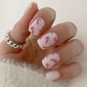 Close-up of matte Christmas press on nails featuring red candy cane designs on cream base