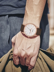 Close-up of minimalist rose gold watch with white dial and date window on brown leather strap