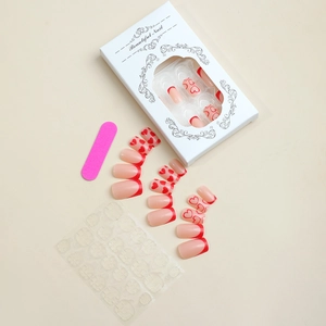 Gros plan d'un kit de faux ongles cœurs rouges avec colle et lime en boîte blanche