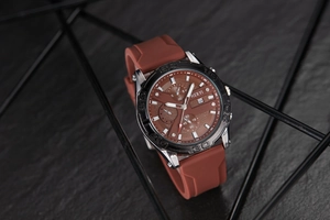 Macro shot of silver metal bezel with embossed numerals and brown silicone watch strap