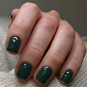 Macro detail of dark ink green handmade press-on nails with high gloss on gray knit fabric