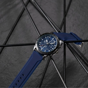 Men's chronograph watch with blue silicone strap and silver case on a modern rock background