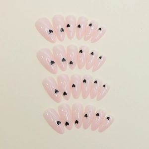 Close-up of almond shaped press-on nails in nude pink with black heart prints