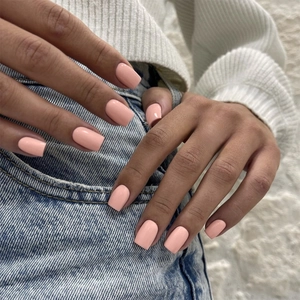 Close-up of light peach short square press-on nails with glossy finish on fingers