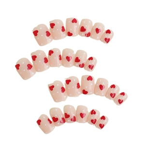Short square press-on nails with nude pink base, red hearts, and white polka dots