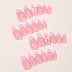 Faux ongles amande rose style français avec nœuds 3D et perles pour un look élégant