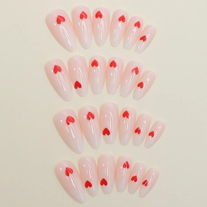 Detail view of almond press-on nails featuring soft pink base and red heart patterns