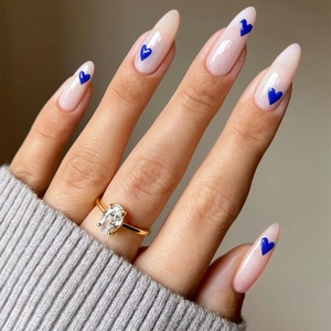 Elegant almond-shaped nude nails with blue heart pattern and gold diamond ring