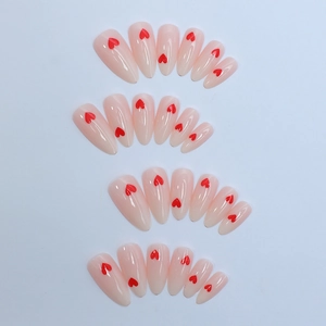 Almond shaped press-on nails in nude pink finish featuring red heart patterns