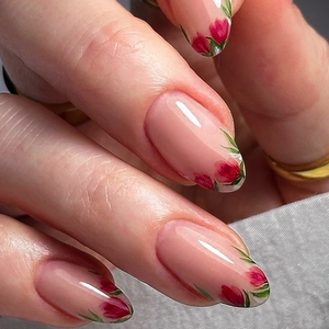 Détail des faux ongles ovales avec motif floral de roses rouges et base rose nude