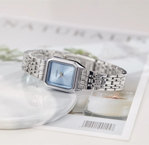 Vue détaillée d'une montre carrée en argent avec cadran bleu clair effet soleil sur marbre