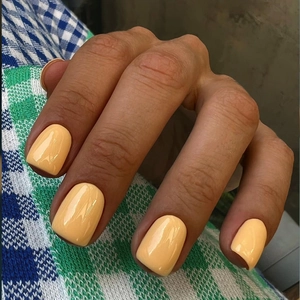 Detail of short square apricot yellow press-on nails with glossy finish on a hand