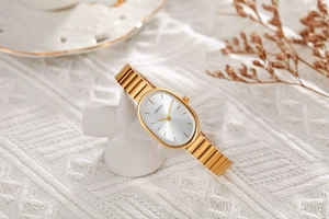 Detail of elegant gold oval quartz watch resting against a white geometric stand