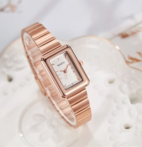 Detailed close-up of rose gold rectangular watch with link strap on a white plate