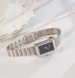 Close-up of rectangular silver watch with black dial and metal chain strap on white surface