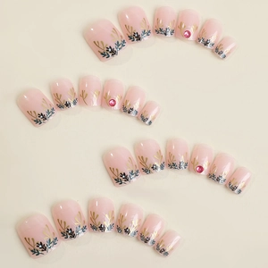 Short square pink press-on nails with golden leaf patterns and small red rhinestones