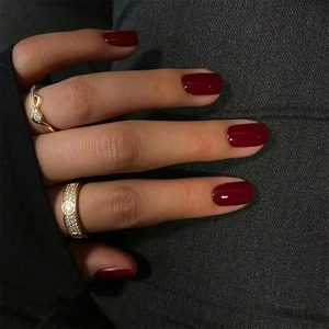 Detail of burgundy red press-on nails paired with a gold pavé screw pattern ring