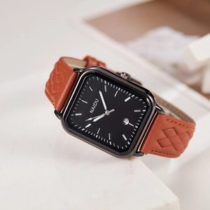 Detail of square watch with black dial and brown leather strap with diamond pattern texture