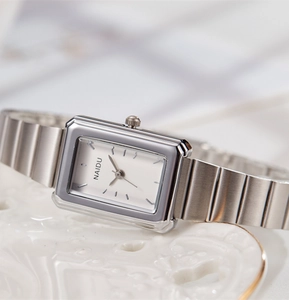 Macro shot of silver rectangular quartz watch with sleek metal band on white ceramic