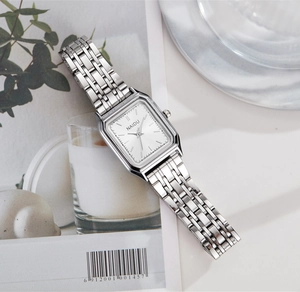 Vue détaillée d'une montre à quartz carrée argentée posée sur une page de magazine épurée