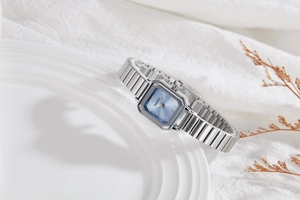Detail shot of a square silver quartz watch with a light blue Roman numeral dial on a plate