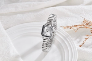 Detail view of a square silver quartz watch with a minimalist Roman numeral dial and band