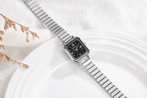 Elegant square silver watch with black dial and Roman numerals on ceramic tray