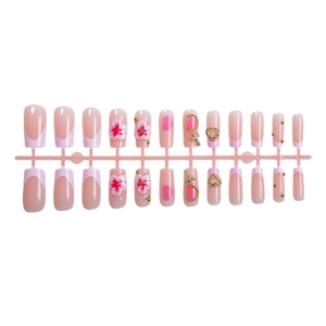 3D floral and heart pattern press-on nails with pink French tips on a display stand