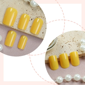 Glossy bright yellow press-on nails set on textured stone with pearl necklace detail