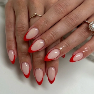 Glossy red French tip almond press-on nails shown on model hand with elegant rings