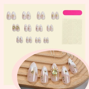 French almond press-on nails with gold starbursts and green heart gemstone accents