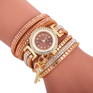 Détail de montre quartz dorée avec lunette en strass et bracelet multicouche à breloque