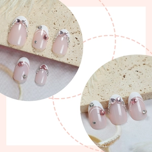 Nude pink press-on nails with white French tips and heart-shaped rhinestone accents