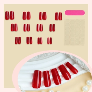 Glossy red press on nails set with adhesive tabs and nail file on a beige background