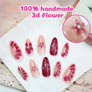 Dettaglio macro di unghie finte a mandorla fatte a mano con fiori 3D e cristalli