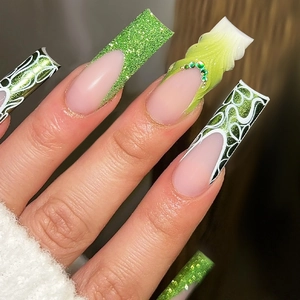 Close-up of long coffin press-on nails with green glitter, 3D relief, and emerald rhinestones