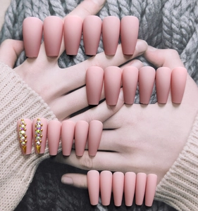 Detail of matte pink ballerina fake nails featuring colorful rhinestones and gold studs