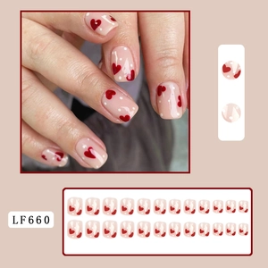 Short square press-on nails with red heart patterns and white dots on a nude pink base
