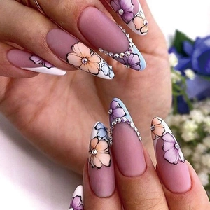 Close-up of matte almond press-on nails with hand-painted flowers and rhinestone accents