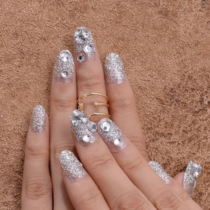 Close-up of silver glitter press-on nails with rhinestone accents and gold star ring