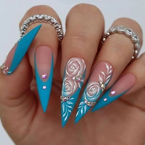 Macro detail of blue stiletto press-on nails with white rose art and small rhinestones