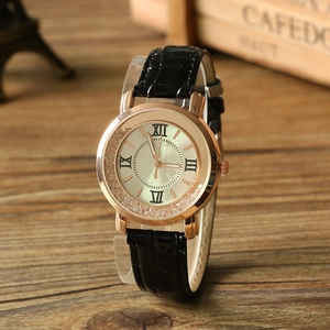 Détail de montre à quartz rose doré avec chiffres romains et bracelet en cuir noir sur bois