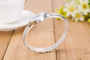 Side view of silver quartz bracelet watch on light wood surface with floral background