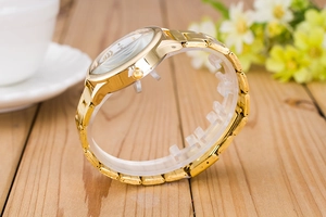 Detail shot of a golden business watch on a wooden table with a coffee cup and flowers