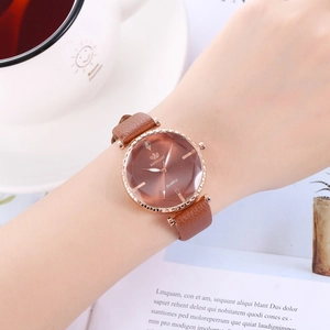 Detail einer kaffeebraunen Lederuhr mit roségoldenem Gehäuse neben Kaffeetasse