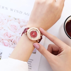 Gros plan d'une montre femme or rose avec cadran rouge et détails en cristaux