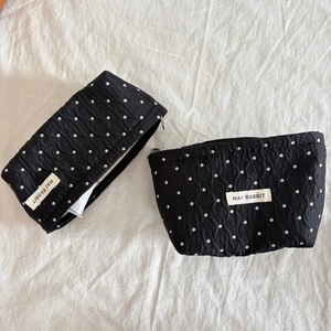Top view of two black polka dot makeup bags with brand label on white fabric
