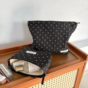 Set of two black polka dot quilted cosmetic bags with white brand tag on a wooden counter